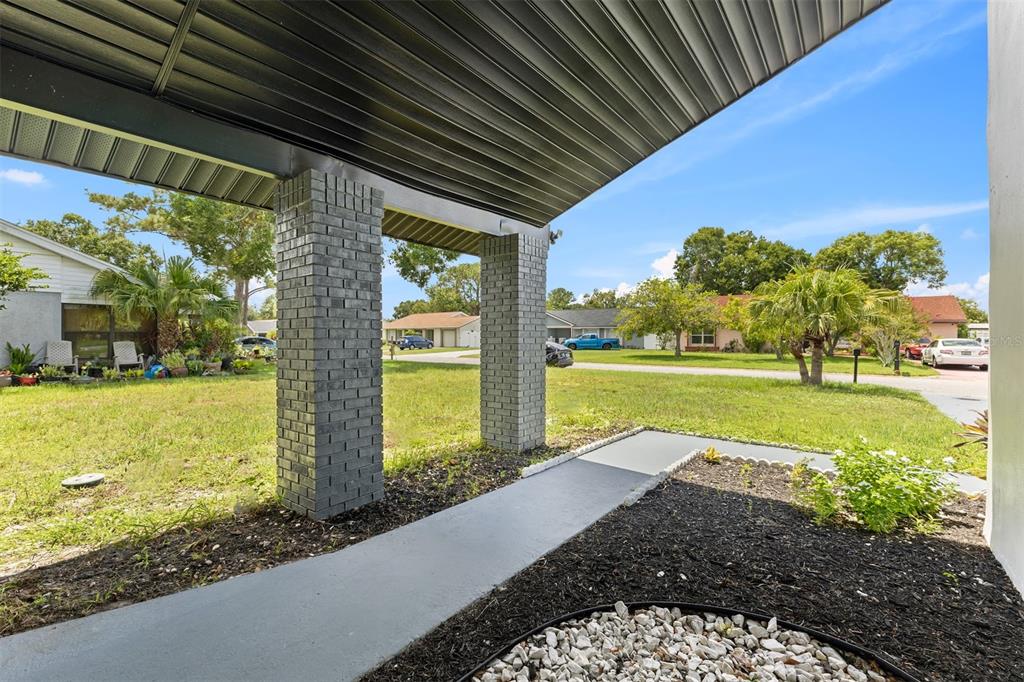 A covered entryway with gray brick columns leads to a concrete walkway in a suburban neighborhood — 17 S FLAG CT, KISSIMMEE, FL