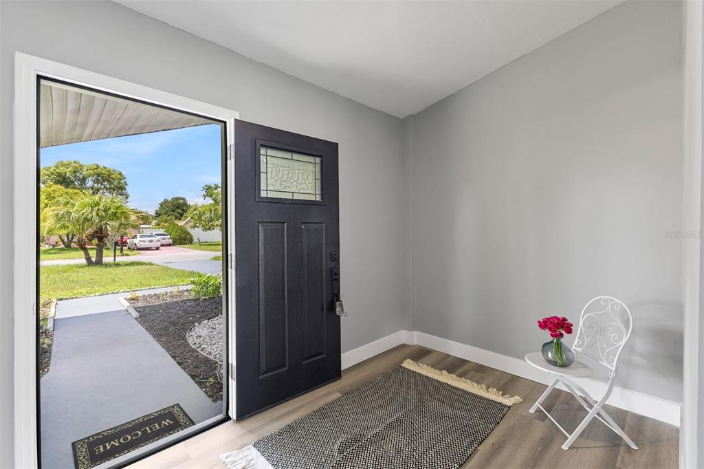 An entryway features a black front door, gray walls, wood-look flooring, and a small chair — 17 S FLAG CT, KISSIMMEE, FL