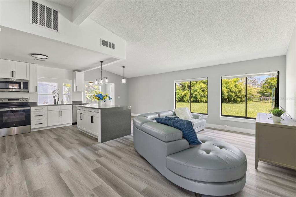An open-concept kitchen and living area with gray wood-look flooring and white cabinetry — 17 S FLAG CT, KISSIMMEE, FL