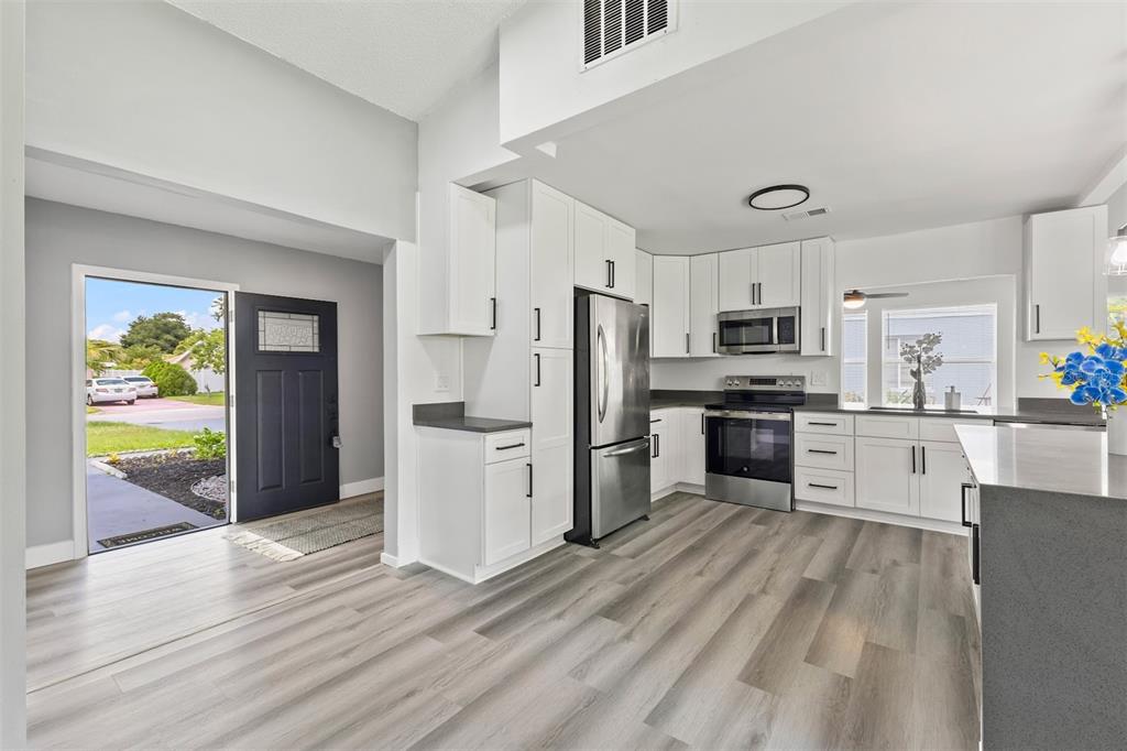 A kitchen with white cabinets, stainless steel appliances, and gray flooring opens to an entryway — 17 S FLAG CT, KISSIMMEE, FL