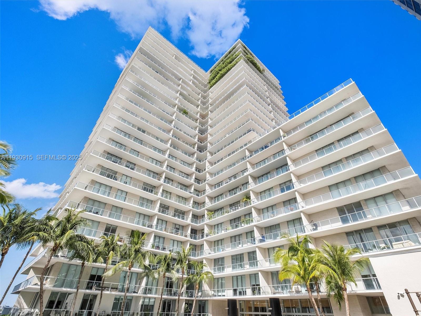 A low-angle view shows a tall, white modern residential building with tiered balconies and palm trees — 3470 E Coast Ave # H1605, Miami FL 33137, MIAMI, FL