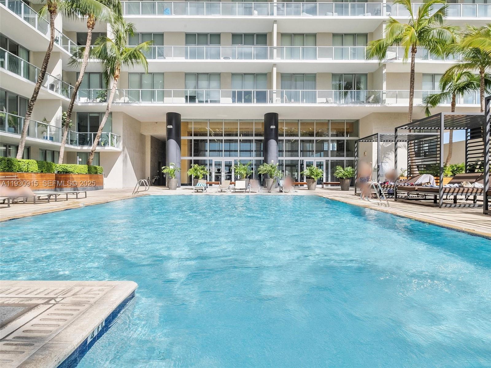 A swimming pool sits in front of a multi-story building with balconies and palm trees — 3470 E Coast Ave # H1605, Miami FL 33137, MIAMI, FL