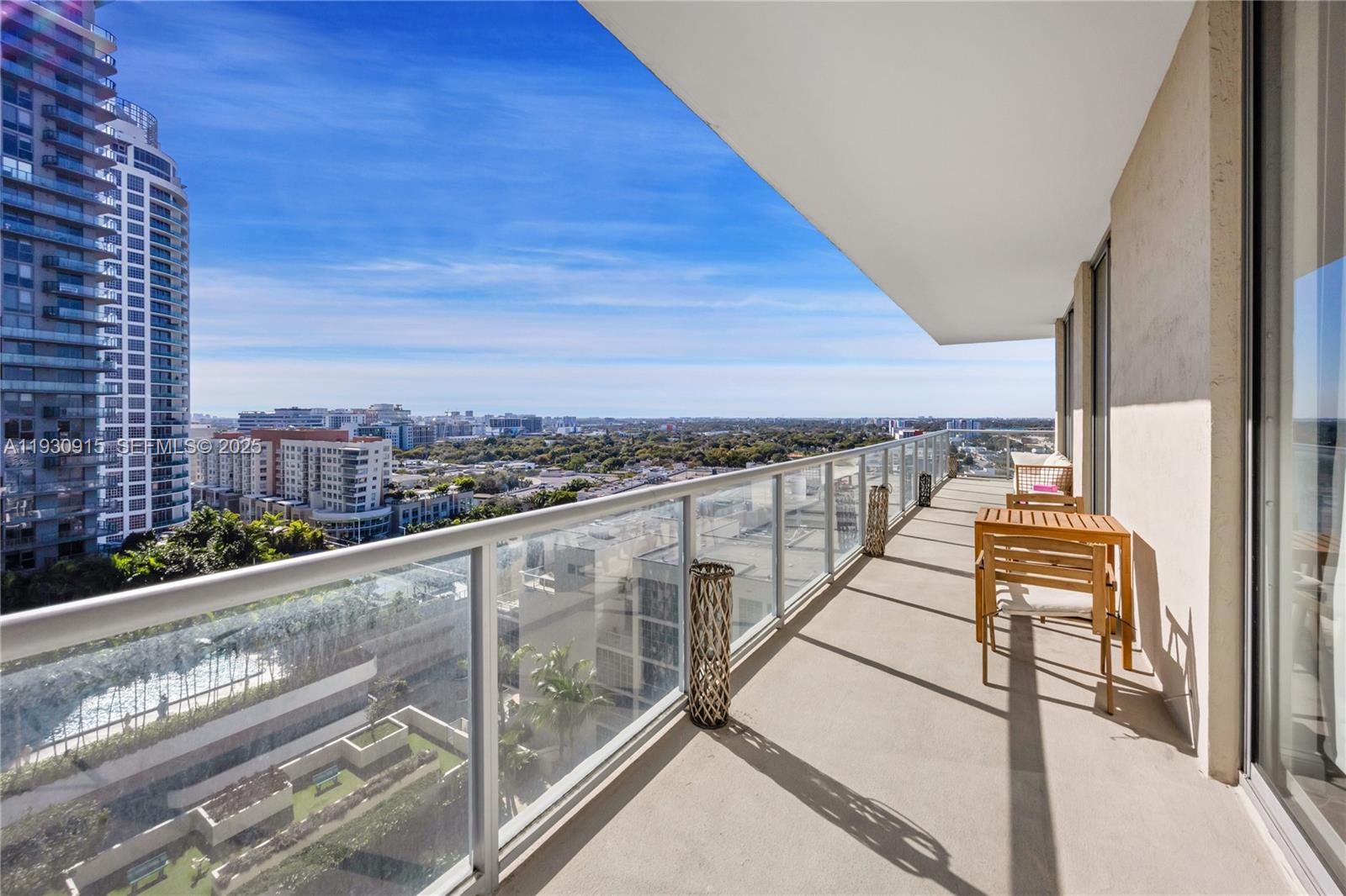 A high-rise balcony features a glass railing, wooden furniture, and a panoramic city view — 3470 E Coast Ave # H1605, Miami FL 33137, MIAMI, FL