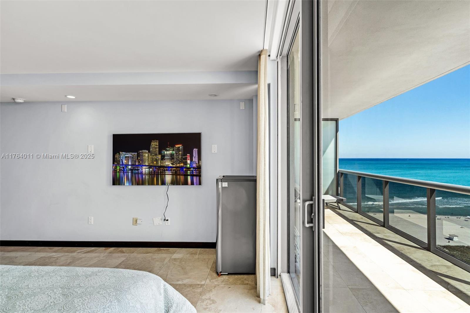 A bedroom features a wall-mounted television, a small refrigerator, and a balcony overlooking the ocean — 5875 Collins Ave # 1704, Miami Beach FL 33140, MIAMI BEACH, FL