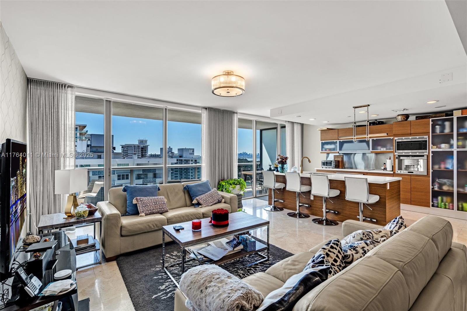 A modern living room and kitchen area features floor-to-ceiling windows with a city view — 5875 Collins Ave # 1704, Miami Beach FL 33140, MIAMI BEACH, FL