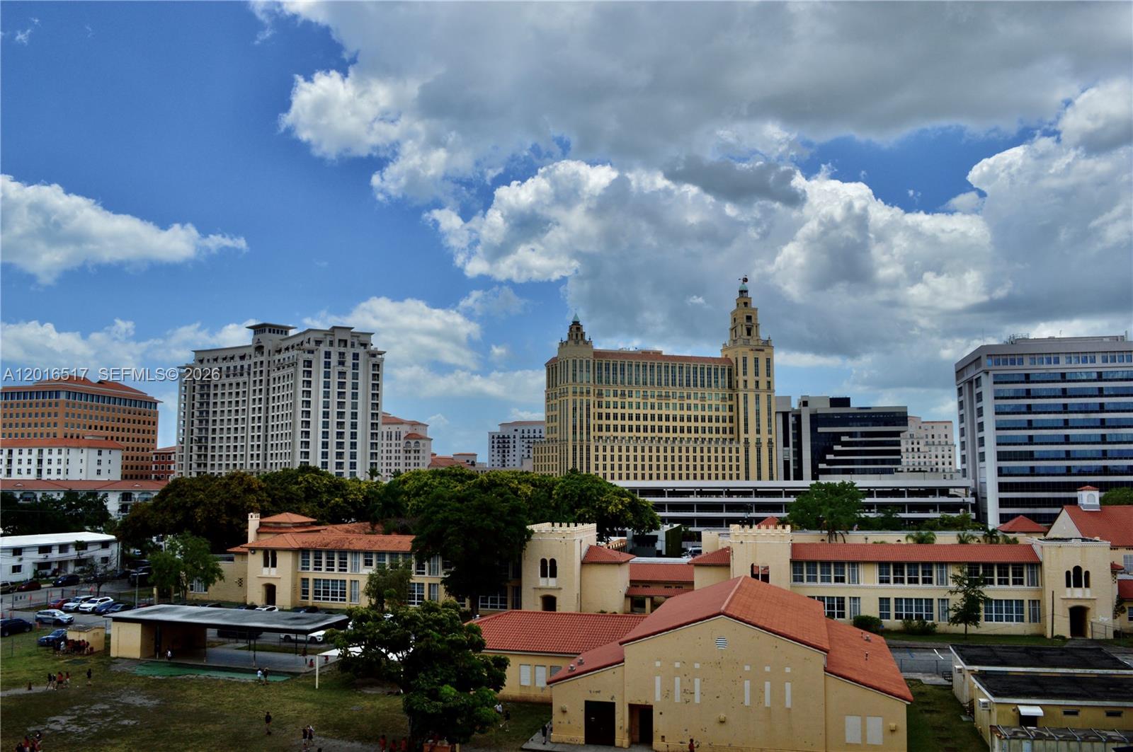 An exterior view shows a school campus in the foreground with city buildings behind it — 1805 Ponce De Leon Blvd # 529, Coral Gables FL 33134, CORAL GABLES, FL