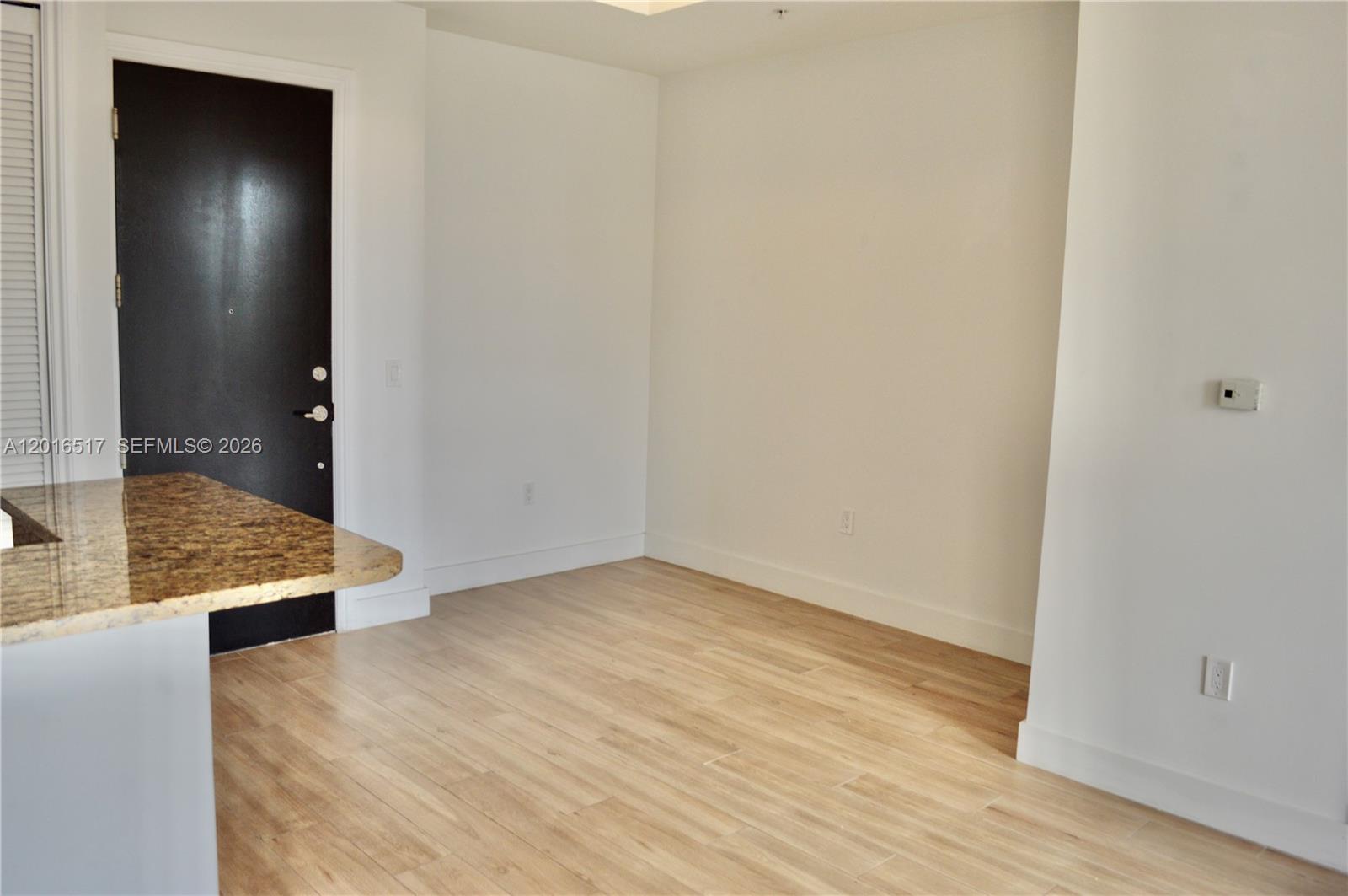 An empty room with light wood flooring, white walls, and a dark entry door — 1805 Ponce De Leon Blvd # 529, Coral Gables FL 33134, CORAL GABLES, FL