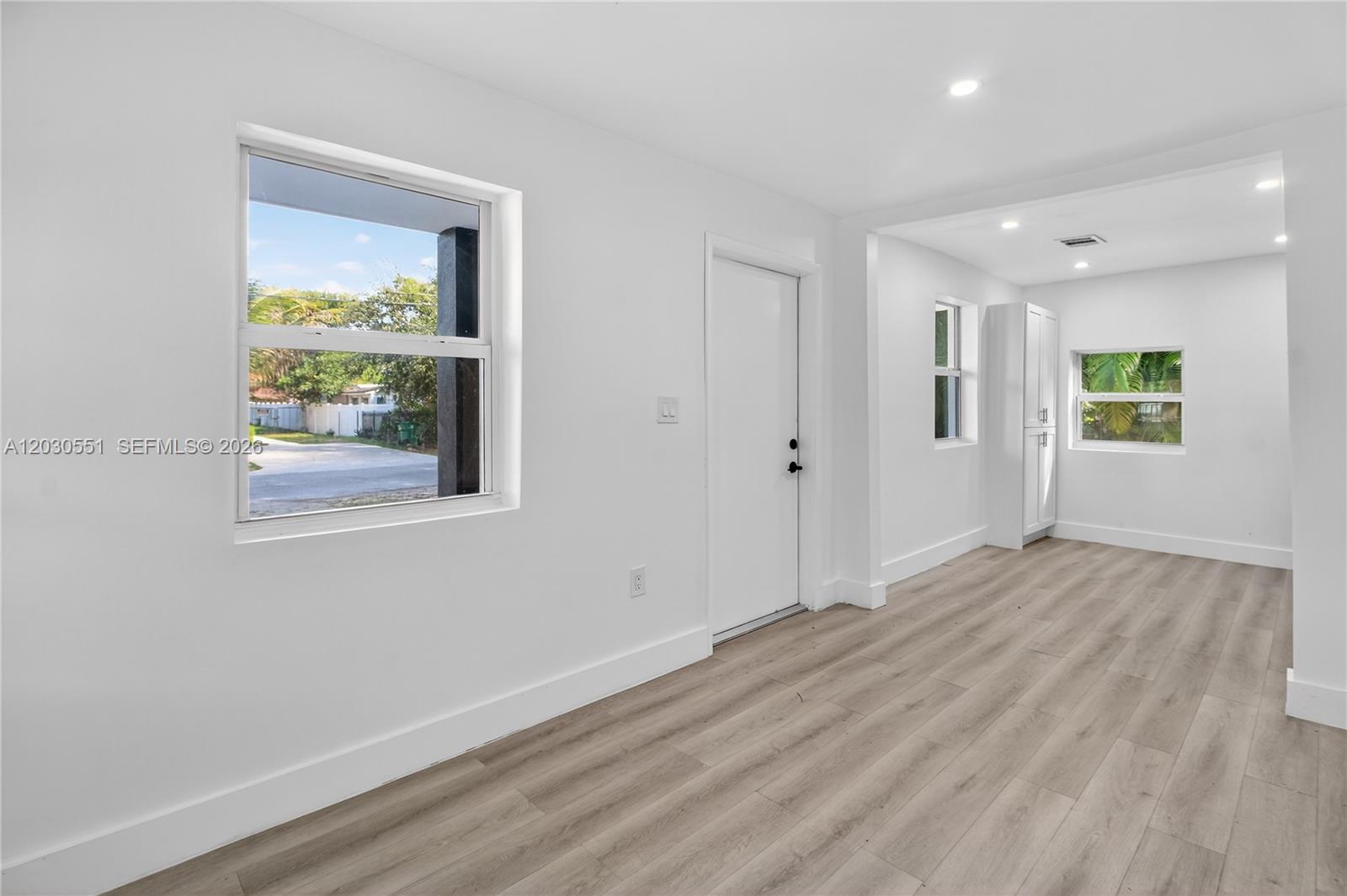 A bright, minimalist room features light wood-look flooring, white walls, and a white door — 428 NW 97th St, Miami FL 33150, MIAMI, FL