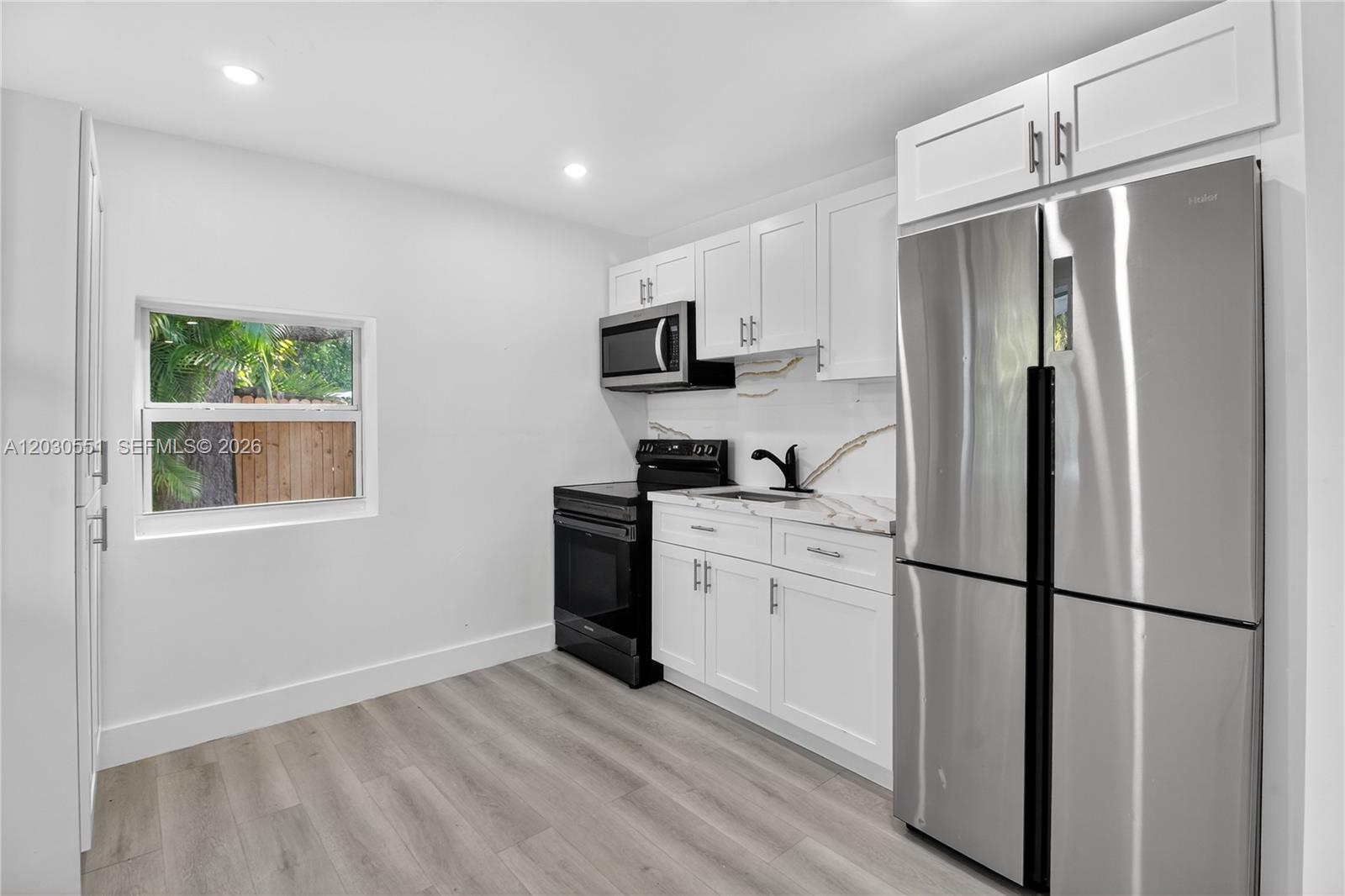 A small kitchen features white cabinets, stainless steel appliances, and light wood-look flooring — 428 NW 97th St, Miami FL 33150, MIAMI, FL