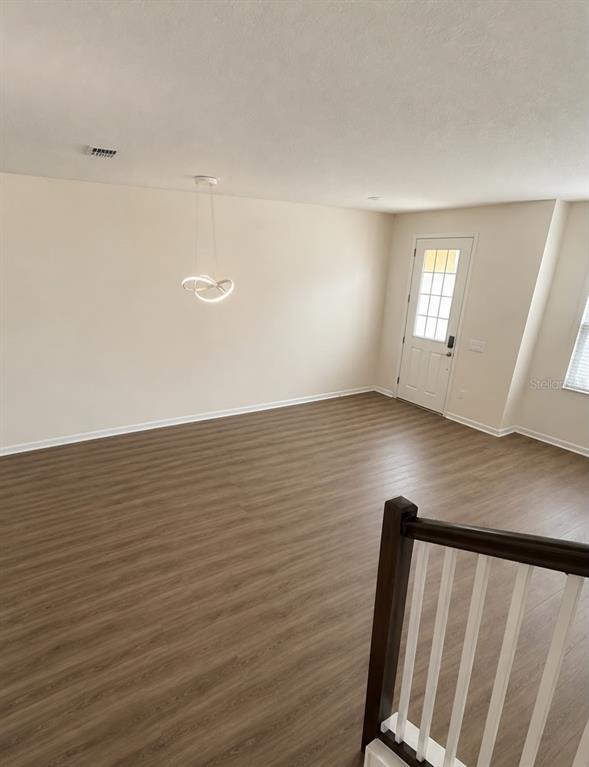 An empty room with light-colored walls, wood-look flooring, a modern pendant light, and a door — 13483 GORGONA ISLE DRIVE, WINDERMERE, FL
