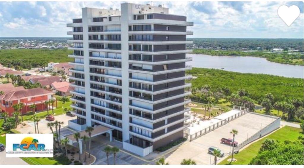 An aerial view shows a coastal road, residential homes, and a high-rise building by the ocean — 1601 CENTRAL AVENUE UNIT 704, FLAGLER BEACH, FL