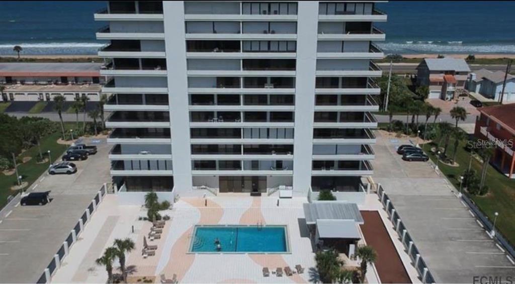 An aerial view of a tall residential apartment building next to a parking lot and water — 1601 CENTRAL AVENUE UNIT 704, FLAGLER BEACH, FL