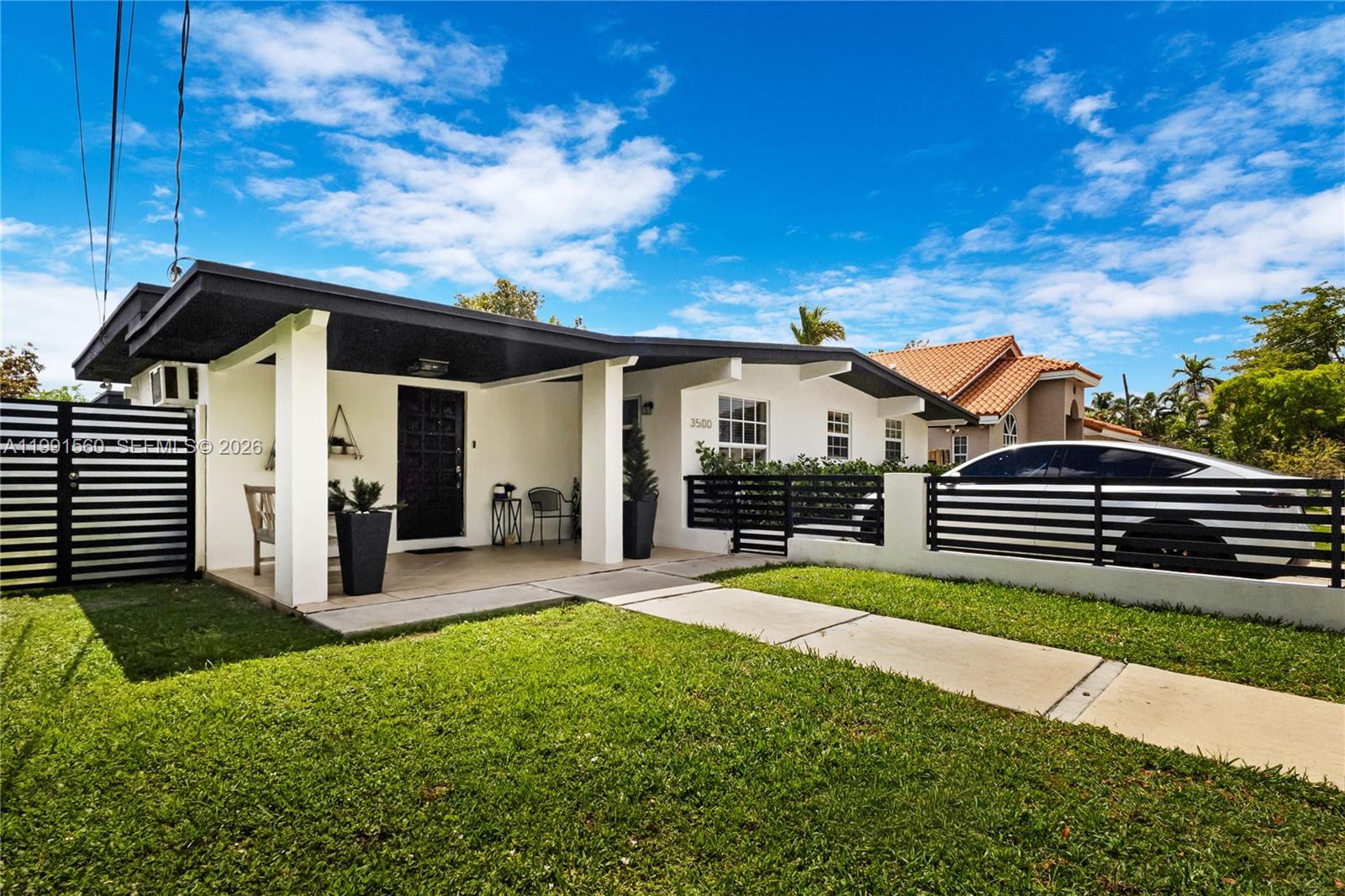 A white single-story house features a black-trimmed roof, a fenced front yard, and two parked cars — 3500 SW 13th St, Miami FL 33145, MIAMI, FL