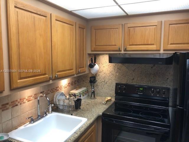 A kitchen features oak cabinets, granite countertops, a white sink, and a black electric stove — 366 Brighton I # 366, Boca Raton FL 33434, BOCA RATON, FL