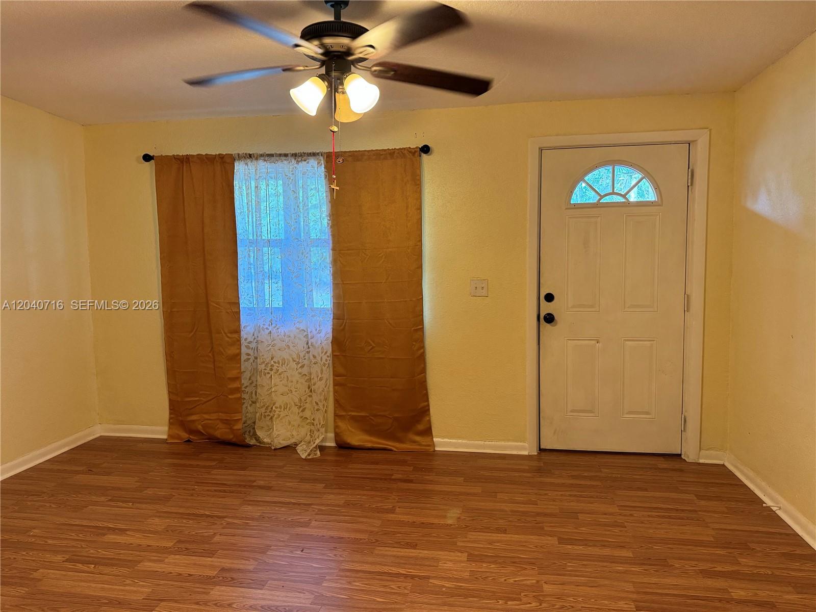 A room with yellow walls, wood-look flooring, a ceiling fan, and a white entry door — 9410 Gilchrist ct, Jacksonville FL 32219, JACKSONVILLE, FL