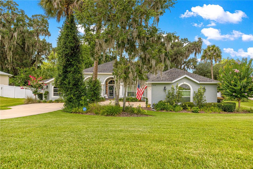 A single-story gray house with a front porch, arched entryway, and a large grassy yard — 2616 SW 18TH AVENUE NE, OCALA, FL