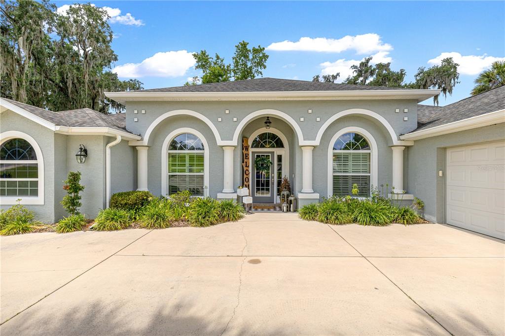 A single-story house with a light green stucco exterior, arched windows, and a concrete driveway — 2616 SW 18TH AVENUE NE, OCALA, FL