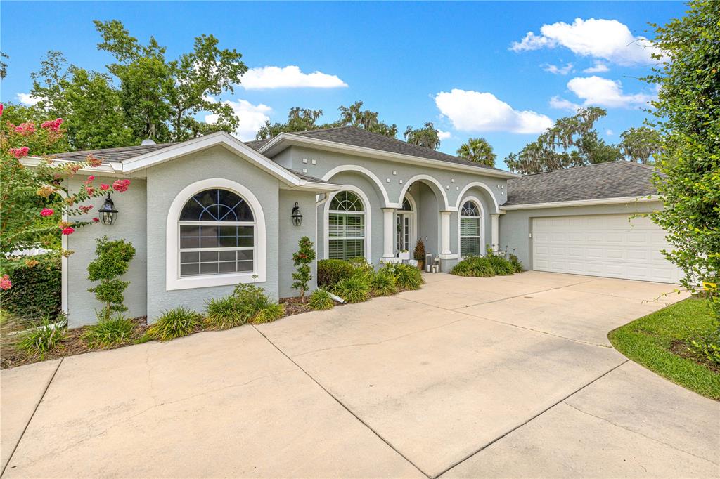 A single-story house with a light gray stucco exterior, arched windows, and a concrete driveway — 2616 SW 18TH AVENUE NE, OCALA, FL