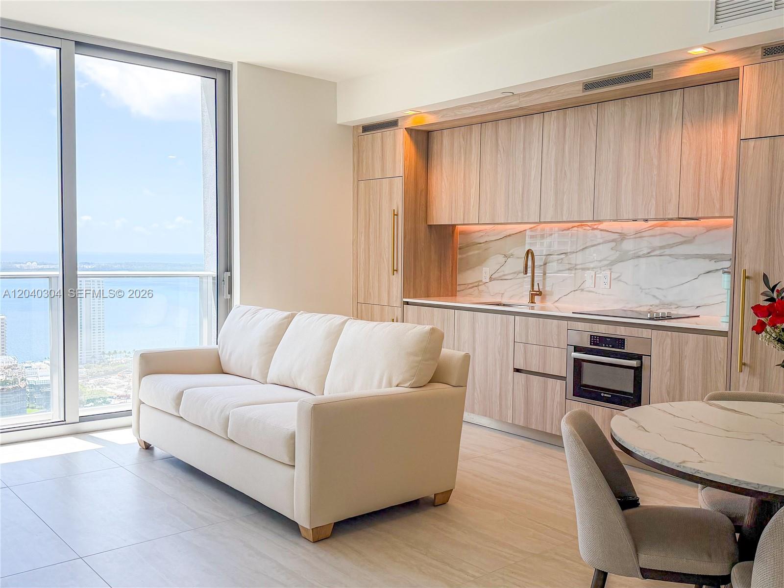 A modern studio apartment features a kitchenette, a white sofa, and a floor-to-ceiling window — 77 SE 5 # 4015, Miami FL 33131, MIAMI, FL
