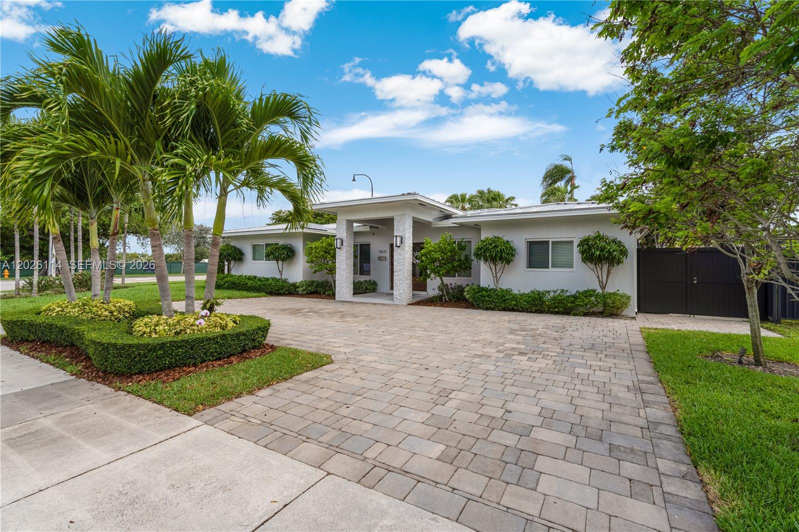 A white single-story house features a paved driveway, palm trees, and manicured landscaping — 9641 SW 66th St, Miami FL 33173, MIAMI, FL