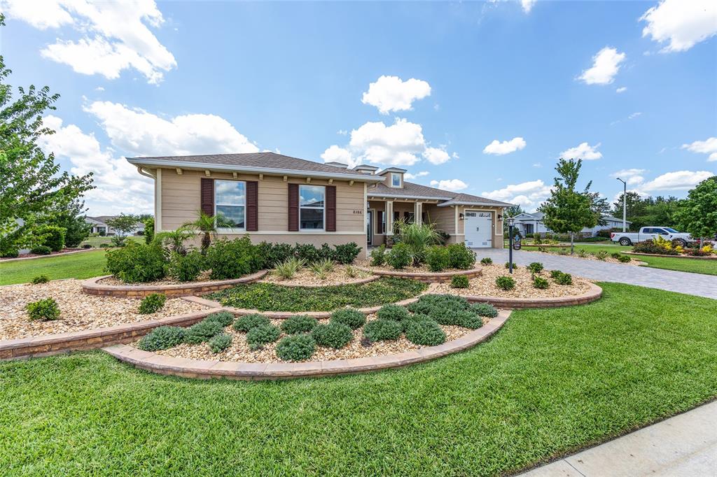 A single-story house with tan siding, brown shutters, and tiered stone-walled landscaping in front — 8386 SW 90TH COURT, OCALA, FL