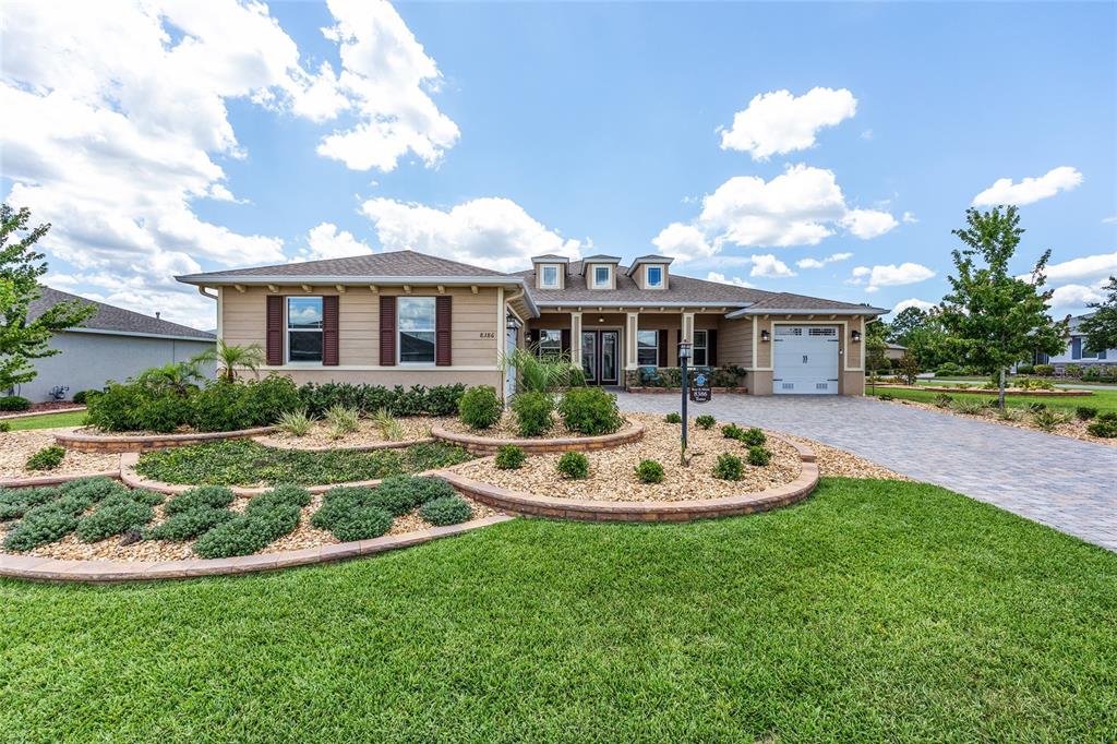 A single-story house with a tan exterior, a paved driveway, and tiered landscaping beds — 8386 SW 90TH COURT, OCALA, FL