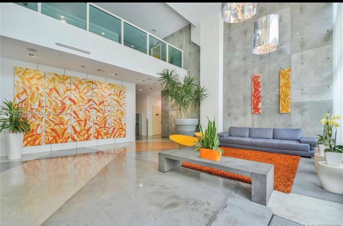 A modern lobby features a high ceiling, concrete walls, a gray sofa, and orange accents — 234 NE 3rd St # 608, Miami FL 33132, MIAMI, FL