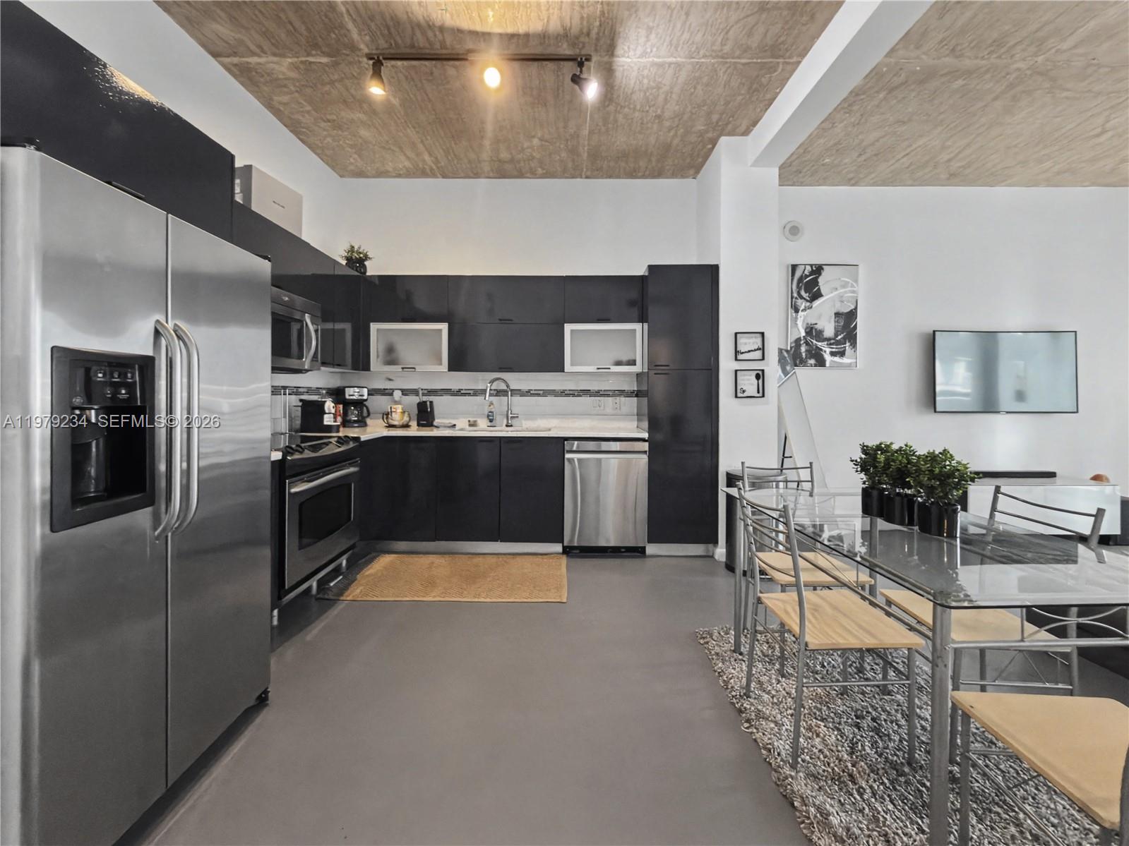 A modern kitchen features dark cabinetry, stainless steel appliances, and a textured concrete ceiling — 234 NE 3rd St # 608, Miami FL 33132, MIAMI, FL