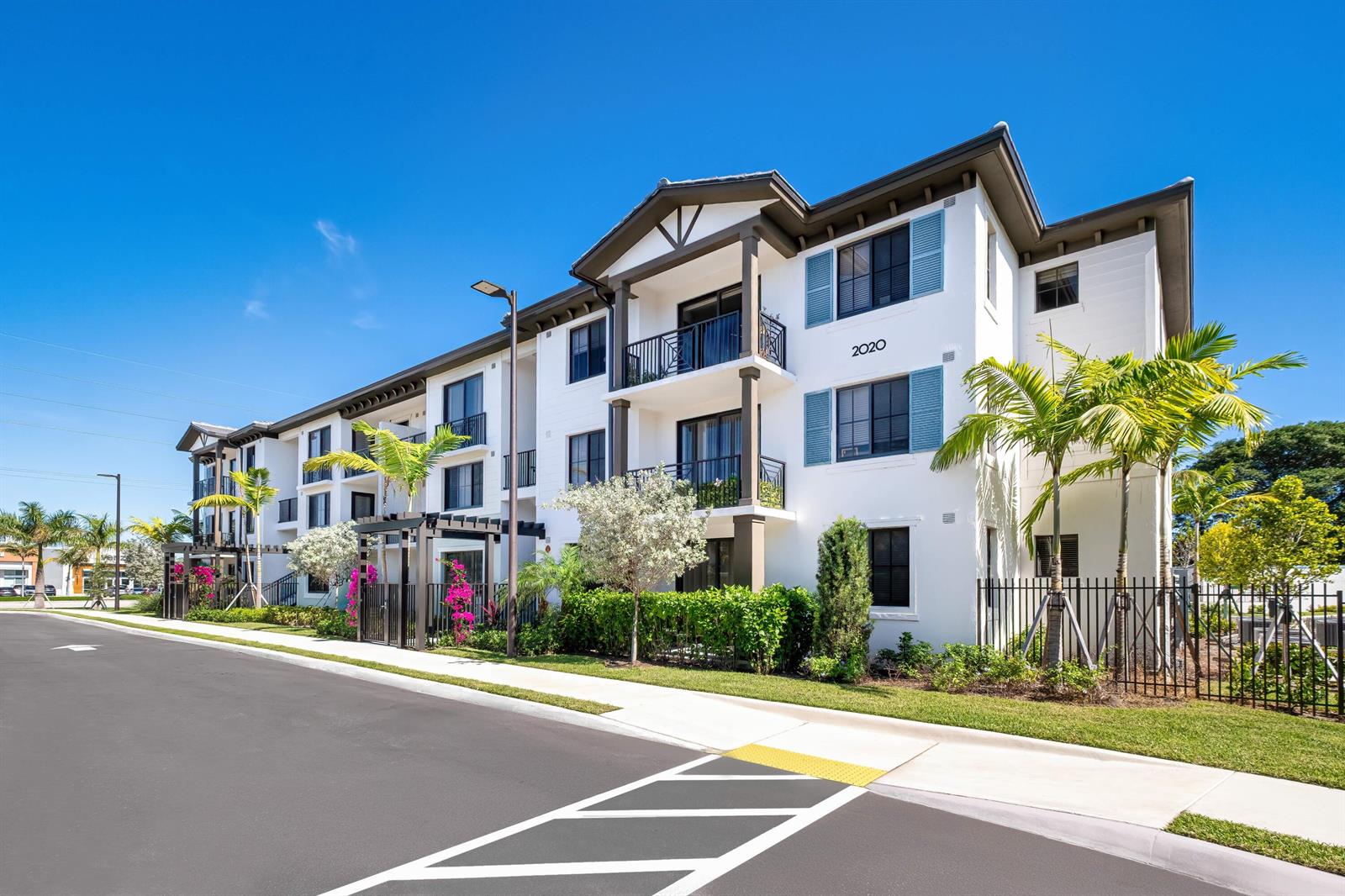 A three-story apartment building with white stucco walls, blue shutters, and palm trees — 2000 Stirling Road # 102, Hollywood FL 33020, HOLLYWOOD, FL