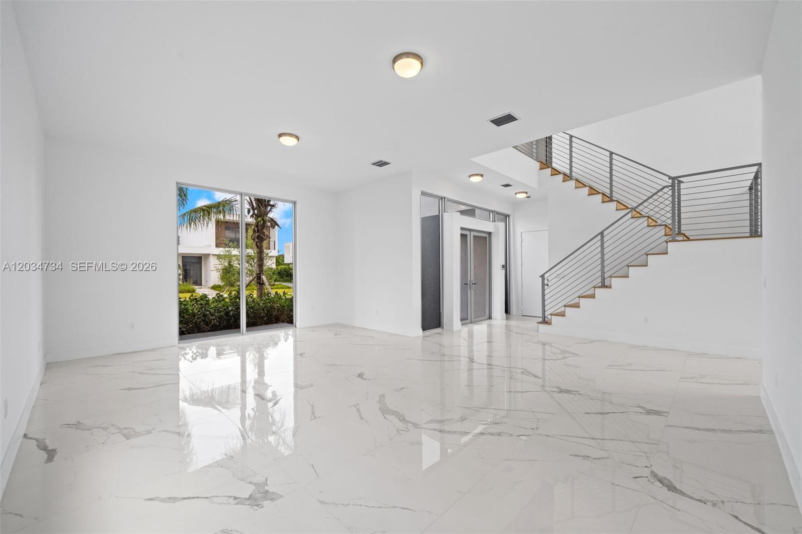 A bright, minimalist living room features white marble floors, recessed lighting, and a floating staircase — 16710 N Botaniko Dr N, Weston FL 33326, WESTON, FL