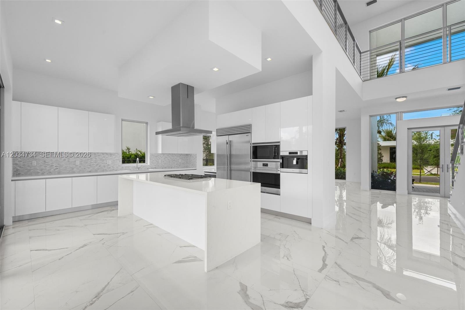 A modern white kitchen features a large island, stainless steel appliances, and marble flooring — 16710 N Botaniko Dr N, Weston FL 33326, WESTON, FL