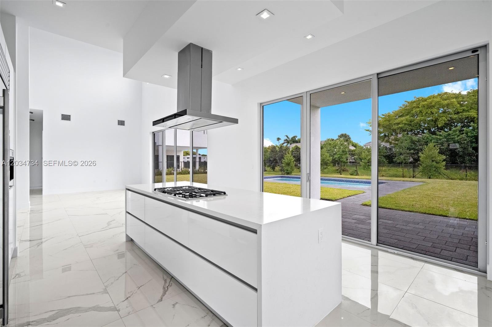 A modern kitchen features a white island with a gas cooktop and marble tile floors — 16710 N Botaniko Dr N, Weston FL 33326, WESTON, FL