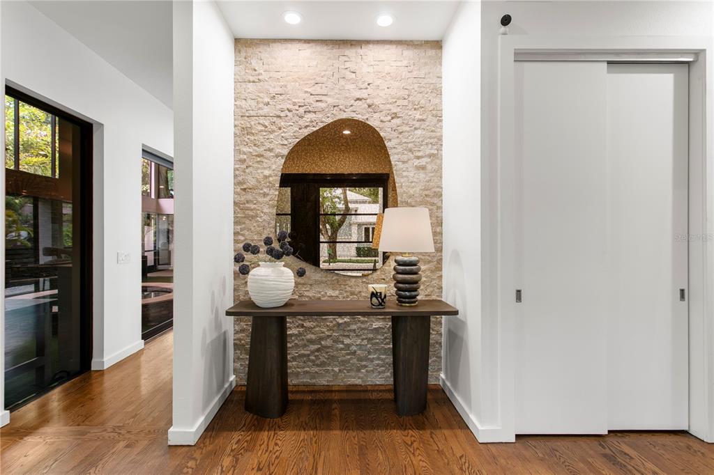 A modern entryway features a stone accent wall, an organic-shaped mirror, and a wooden console table — 2515 W SHELL POINT ROAD, TAMPA, FL