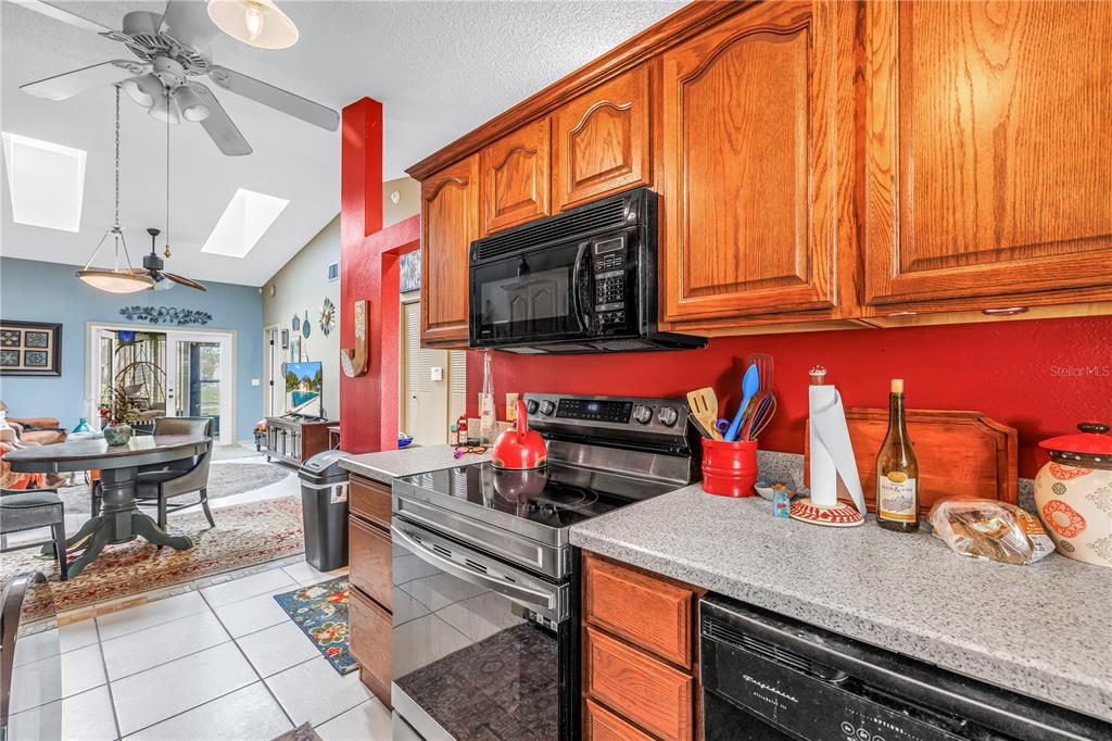 A kitchen with wood cabinets, stainless steel appliances, and red walls overlooks a dining area — 2932 64TH STREET W UNIT 2932, BRADENTON, FL