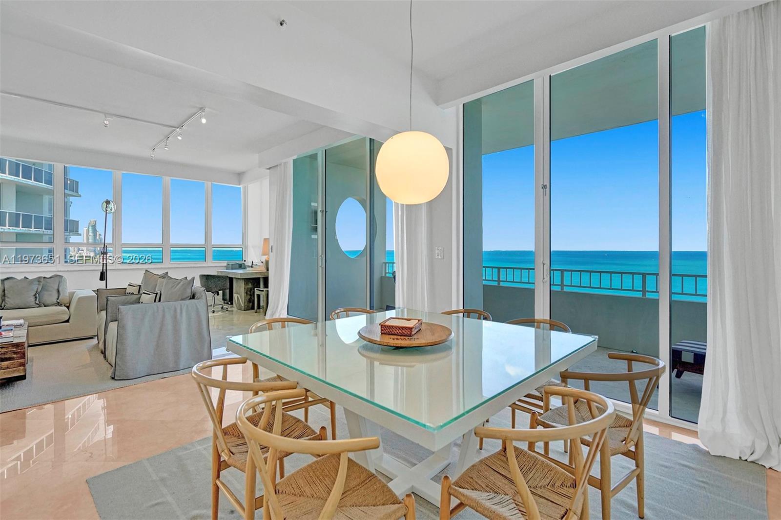 A dining area with a glass table and wooden chairs overlooks the ocean from balconies — 10205 Collins Ave # P8, Bal Harbour FL 33154, BAL HARBOUR, FL