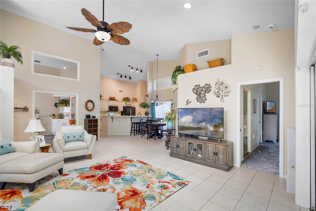 A bright open-concept living room features vaulted ceilings, tile flooring, and a view into the kitchen — 7815 GENEVA LANE, SARASOTA, FL
