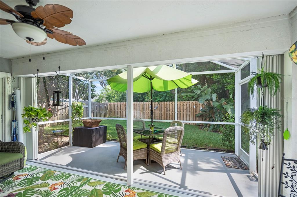 A screened-in patio features a ceiling fan, wicker furniture, a green umbrella, and backyard views — 7815 GENEVA LANE, SARASOTA, FL