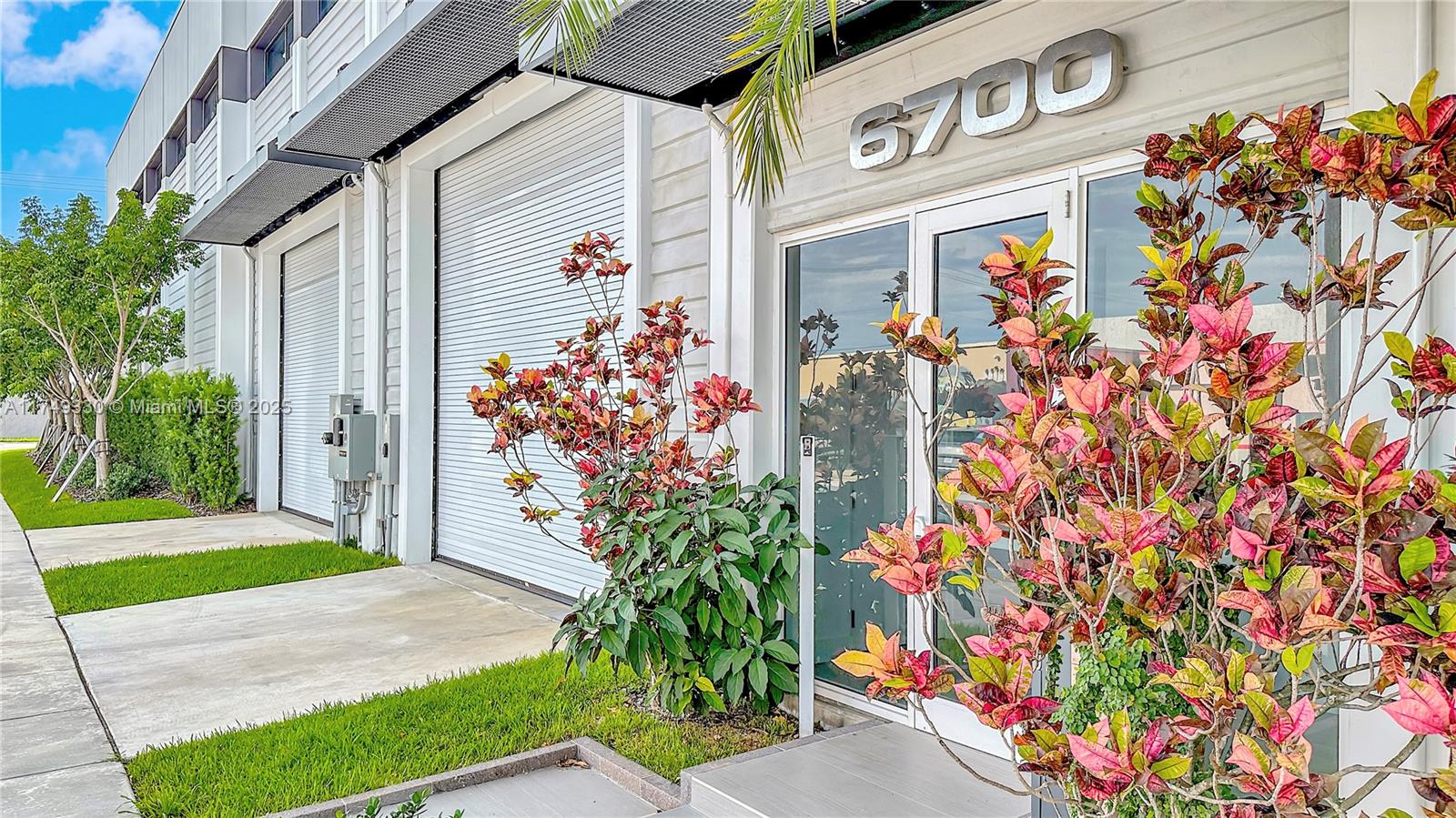 The exterior of a commercial building features a glass entrance door and two roll-up doors — 6700 NE 2nd Ct # 4, Miami FL 33138, MIAMI, FL