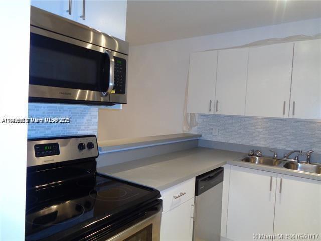 A kitchen with white cabinets, stainless steel appliances, a gray countertop, and a tiled backsplash — 15205 NE 6th Ave # D212, Miami FL 33162, MIAMI, FL