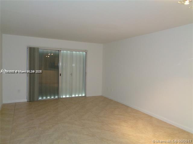 An empty room features white walls, light-colored tile flooring, and a sliding glass door — 15205 NE 6th Ave # D212, Miami FL 33162, MIAMI, FL