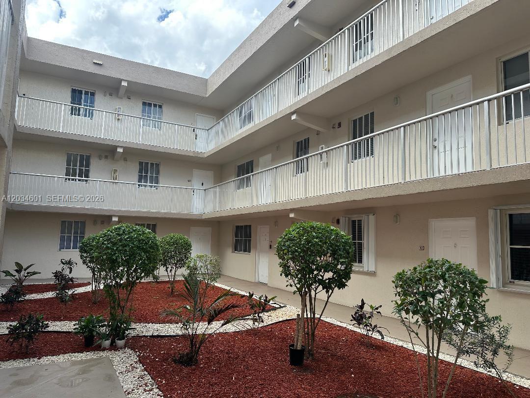 The exterior of a three-story apartment building features white railings and a landscaped courtyard — 6175 NW 186th St # 110, Hialeah FL 33015, HIALEAH, FL