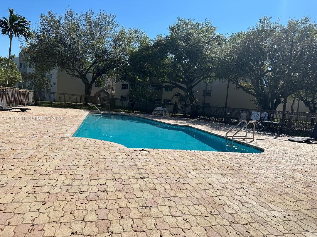 An outdoor swimming pool is surrounded by a paved deck and mature trees — 6175 NW 186th St # 110, Hialeah FL 33015, HIALEAH, FL