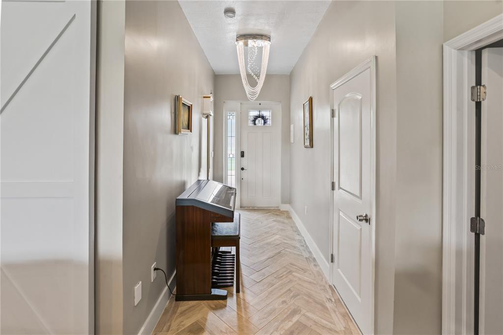 A hallway with herringbone wood-look flooring, a crystal chandelier, and an upright piano — 306 CALENDAR STREET, PORT CHARLOTTE, FL