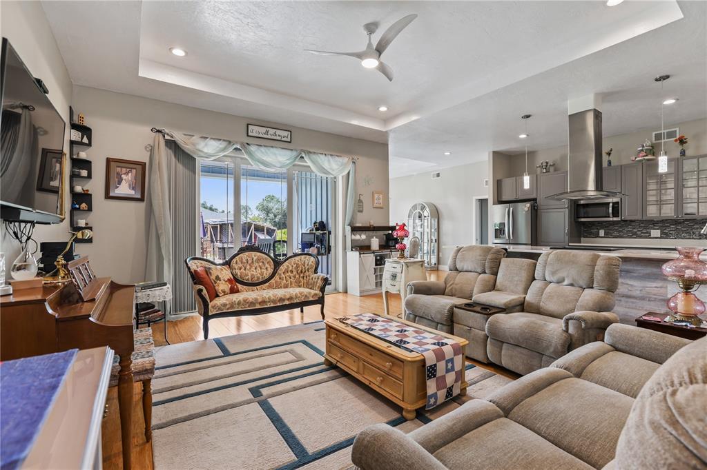 A living room with a piano, sofa, recliner set, and an open kitchen in the background — 306 CALENDAR STREET, PORT CHARLOTTE, FL