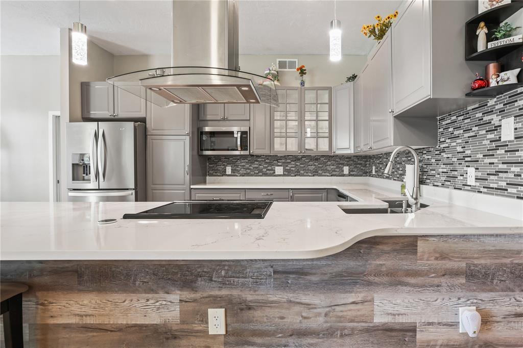 A modern kitchen features gray cabinets, a white quartz countertop, and a wood-paneled island — 306 CALENDAR STREET, PORT CHARLOTTE, FL