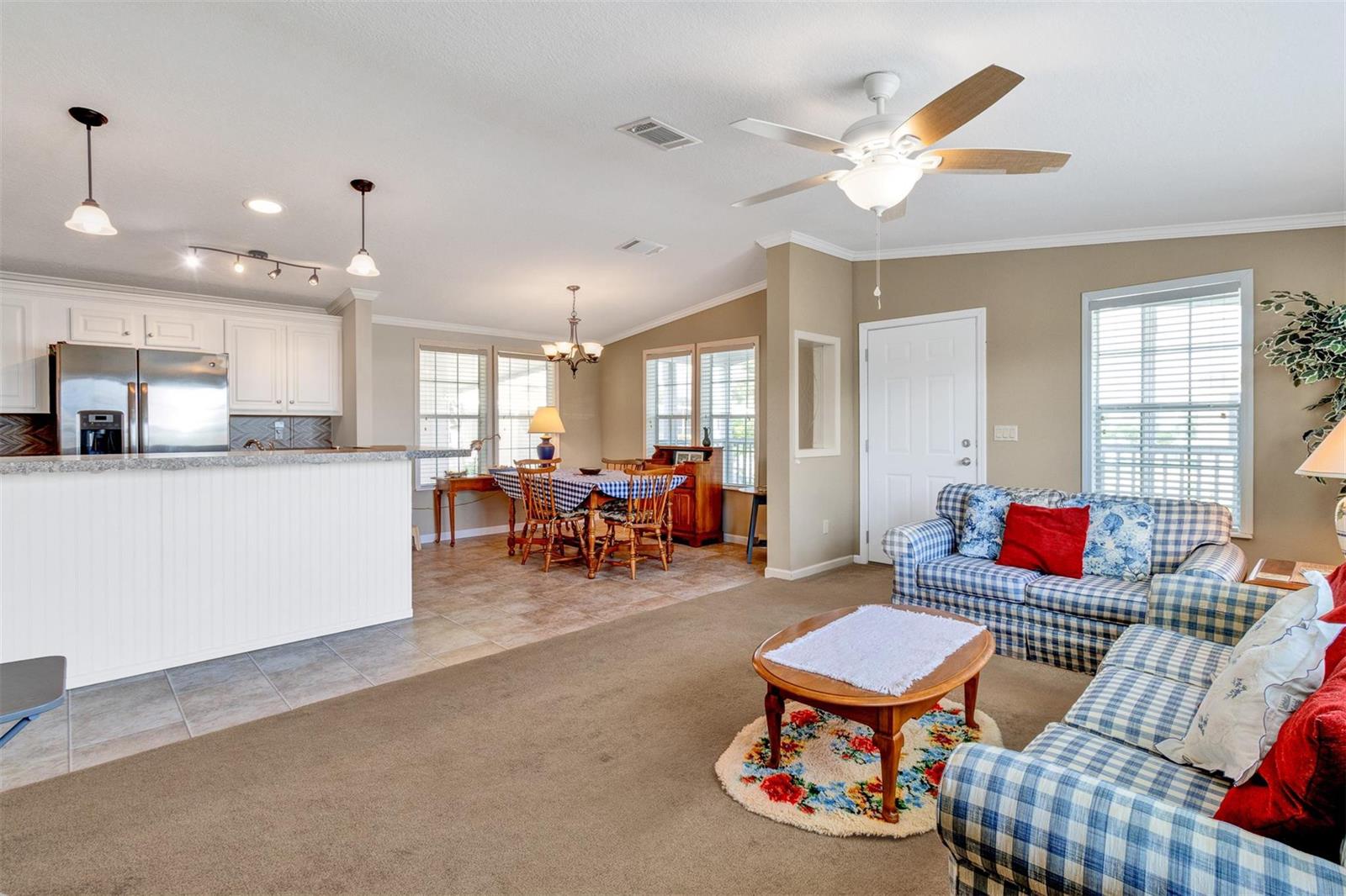 An open-concept living and dining area features a kitchen island, carpeted floors, and plaid furniture — 192 N Arbor Lane, Vero Beach FL 32960, VERO BEACH, FL