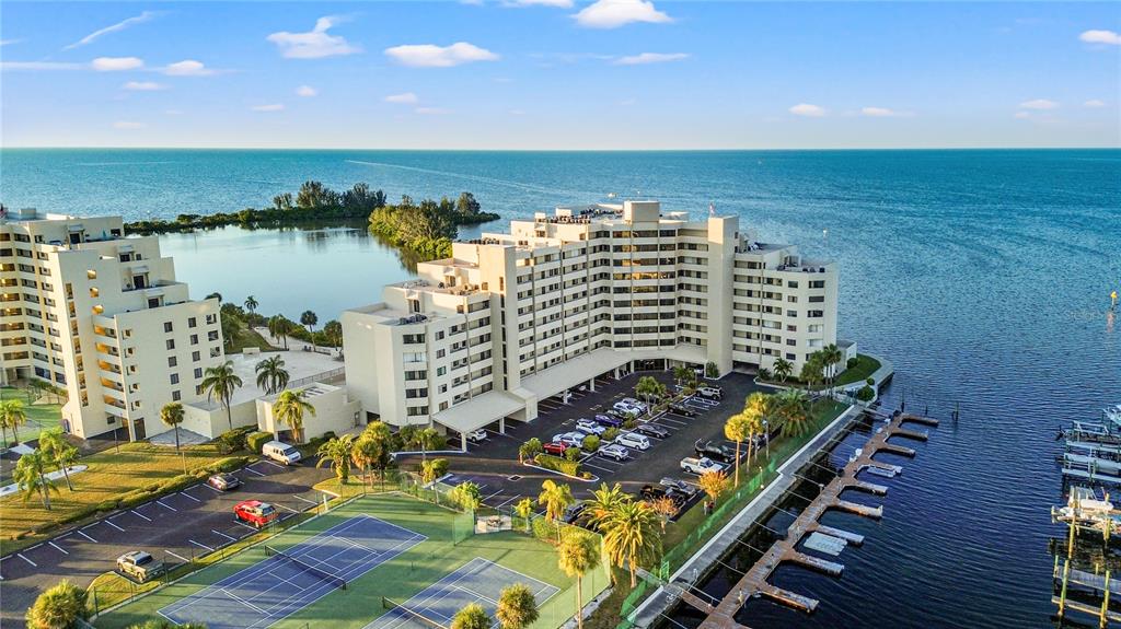 An aerial view shows a multi-story waterfront apartment complex with tennis courts and a boat dock — 6035 SEA RANCH DRIVE UNIT 415, HUDSON, FL