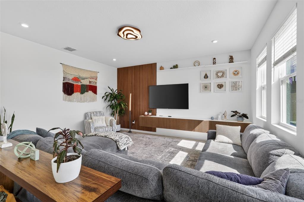 A living room features a grey sectional sofa, a wall-mounted TV, and wood-slat accent paneling — 1181 LAKESHORE BREEZE PLACE, KISSIMMEE, FL