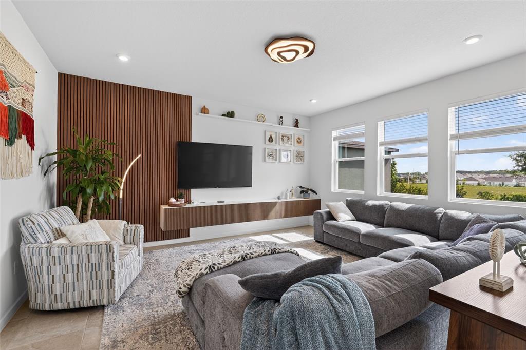 A living room features a slatted wood accent wall, floating media console, and gray sectional — 1181 LAKESHORE BREEZE PLACE, KISSIMMEE, FL