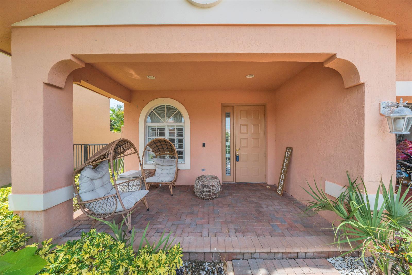 A covered front porch features brick pavers, two wicker egg chairs, and a wooden welcome sign — 149 Bellezza Terrace, Royal Palm Beach FL 33411, ROYAL PALM BEACH, FL
